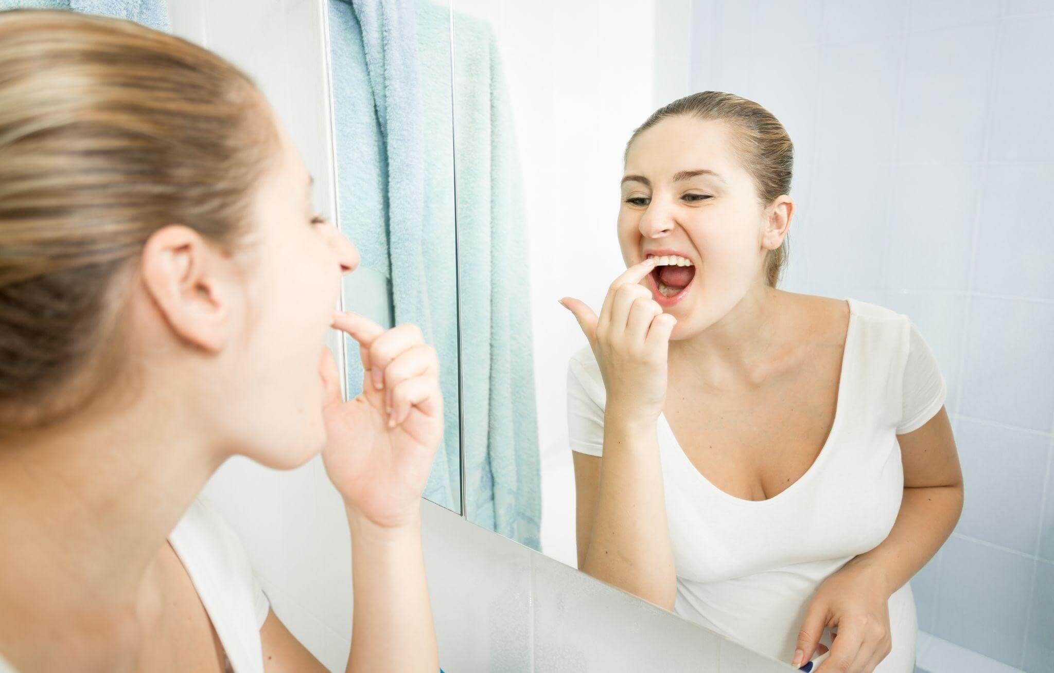 Девушка рассматривает зубы в зеркале